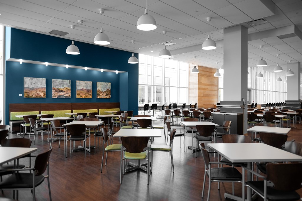 Interior architectural photography of a modern dining area featuring tables, chairs, and blue accent wall with artwork in a well-lit space.