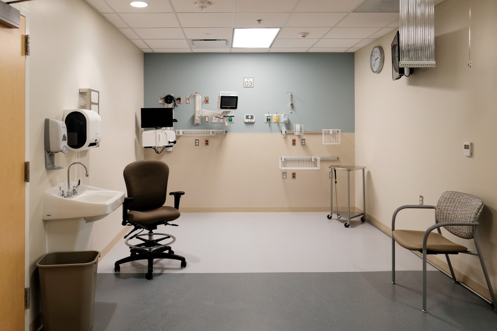 Interior architectural photography of modern hospital treatment room with medical equipment and workspace design.